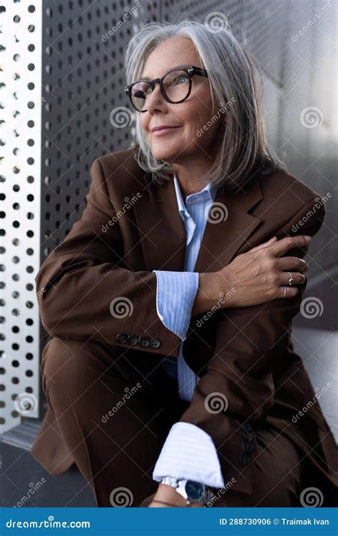 well groomed elderly gray haired business woman in a brown jacket and trousers walks in an urban