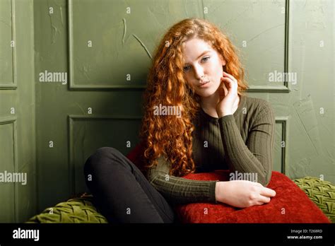 Curly Redhead Girl Sitting At The Sofa Around The Pillows In The Green