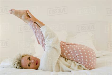 Mature Woman Lying On Bed Stretching Legs Stock Photo Dissolve