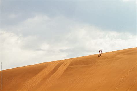 Two Adventurous People At The Top Of A Sand Dune In The Desert By