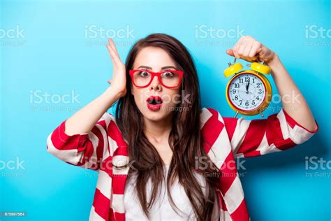 Beautiful Surprised Young Woman With Alarm Clock Standing In Front Of
