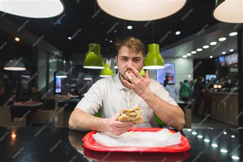 Premium Photo Handsome Man Eats A Burger In A Fast Food And Licks His