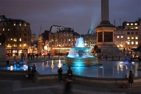 People Are Walking Around In Front Of A Fountain With Lights On It At