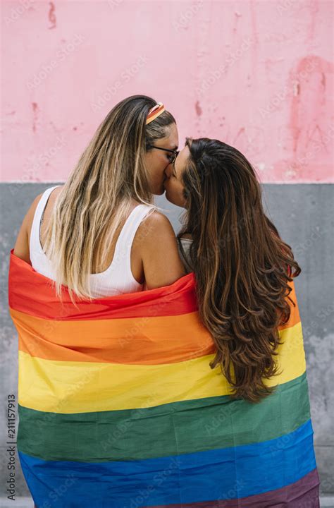 Lesbian Couple Wrap In Gay Pride Flag Kissing Each Other Outdoors Stock