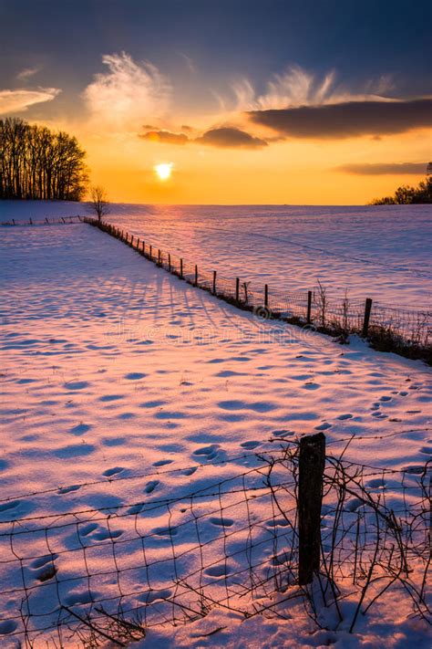 Sunset Over A Fence In A Snow Covered Farm Field In Rural Carrol Stock