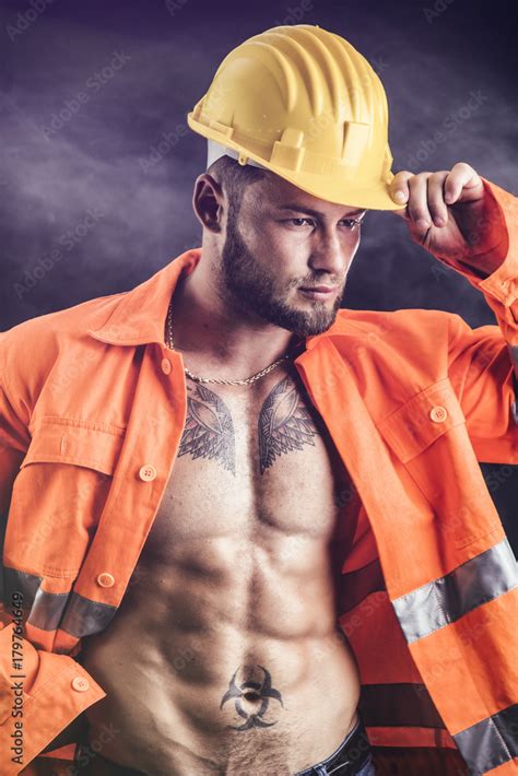 handsome sexy construction worker with orange suit open on naked torso wearing yellow hardhat