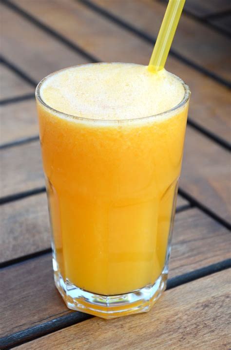 An Orange Drink Sitting On Top Of A Wooden Table With A Straw In Its Mouth