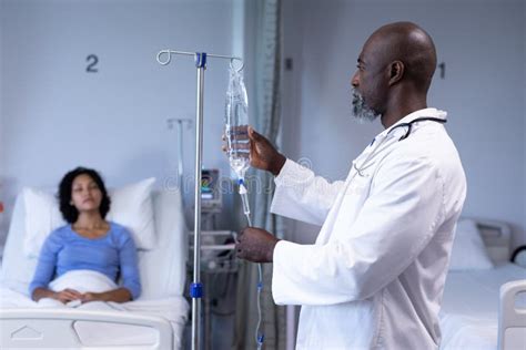 african american male doctor preparing iv drip bag for mixed race woman sitting up in hospital