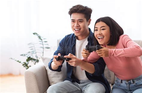 Excited Asian Couple Playing Videogames Sitting On Couch At Home Stock Image Image Of Couple
