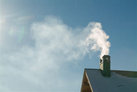Smoke Billows From A Chimney From A House With An Old Roof Over The