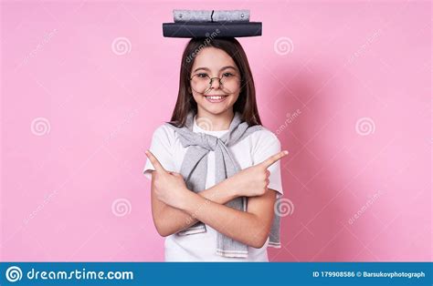 Cute Young Funny Schoolgirl In Glasses Holds Books On Her Head On A