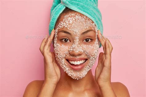 Headshot Of Lovely African American Woman Massages Face Applies Natural Scrub Mask Cleans