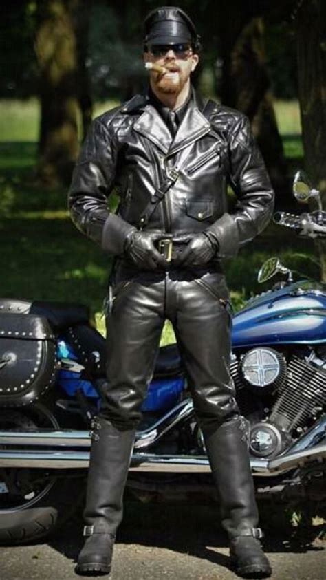 A Man In Leather Clothes Standing Next To A Motorcycle