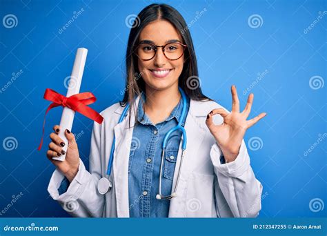 Young Beautiful Brunette Doctor Woman Wearing Glasses And Coat Holding Diploma Degree Doing Ok