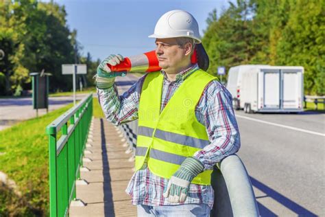 Road Construction Worker With Traffic Cone On Shoulder Near Highway