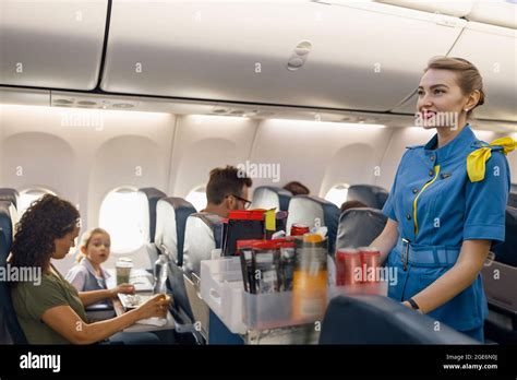 female flight attendant serving food to passengers on aircraft hostess walking with trolley on