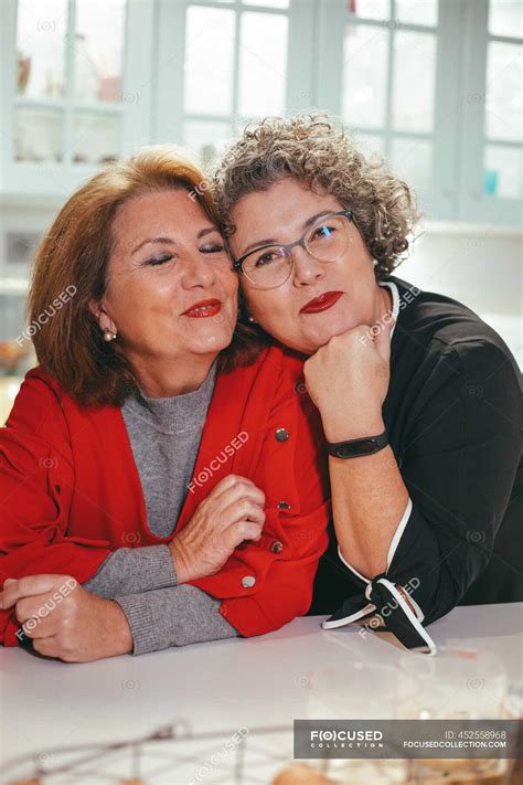 glad middle aged lesbian woman leaning on shoulder of smiling female beloved in house looking at