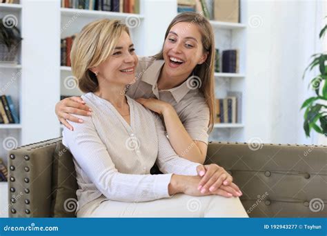 beautiful middle aged mom and her adult daughter are hugging looking at camera and smiling