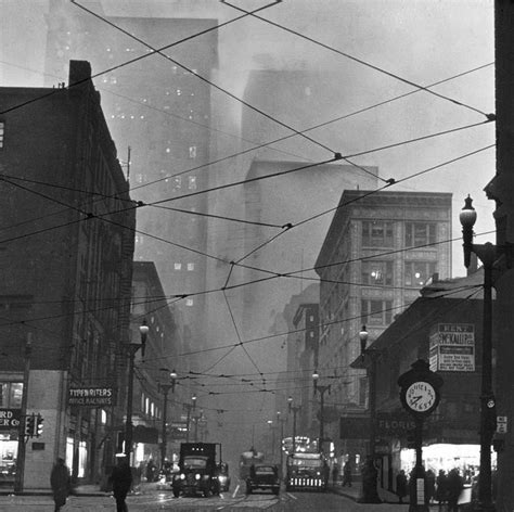 A Black And White Photo Of People Walking On A City Street With Wires