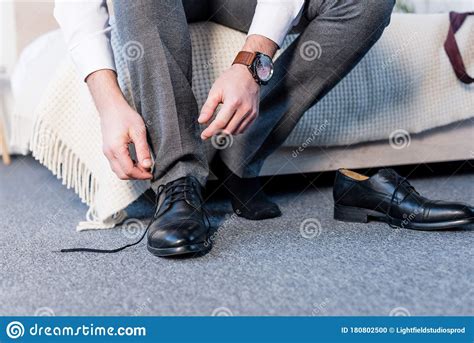Partial View Of Man Putting On Black Leather Shoes While Sitting On