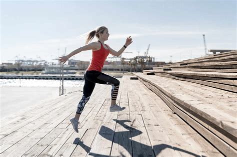 Female Jogger Doing Warm Up Exercise On Steps During Sunny Day Stock Photo