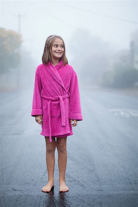 barefoot girl in pink bathrobe stands on a wet street on a foggy morning in portland oregon