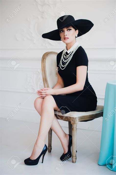 Elegant Woman In Black Dress With A Hat Sitting On A Chair Stock Photo