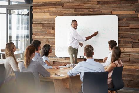 Young Black Man Stands At Whiteboard Addressing Team At Meeting Stock