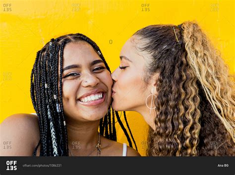 Portrait Of A Beautiful Latin Woman Kissing A Black Woman With Braids With A Yellow Background