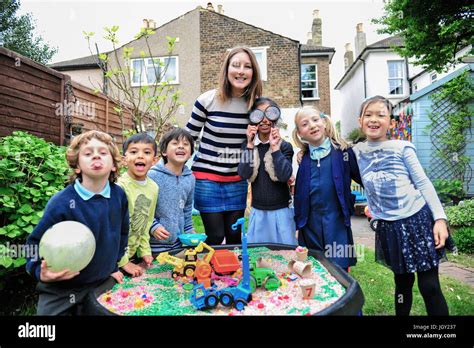 Portrait Of Childminder And Children By Sandpit Looking At Camera
