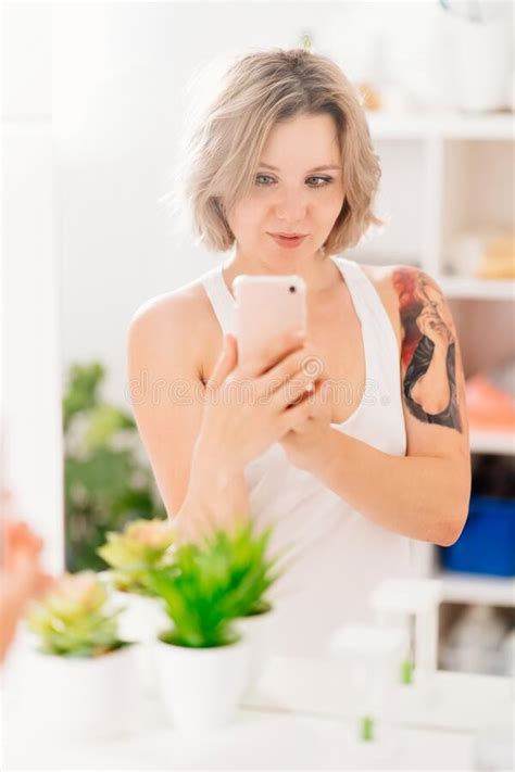 chica sexy con tatuajes tomando foto selfie por teléfono en el espejo del baño imagen de archivo