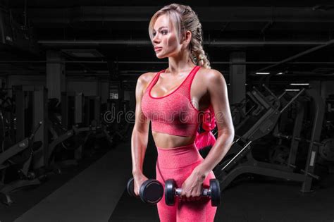 busty blonde in a pink tracksuit posing in the gym with dumbbells fitness concept stock image
