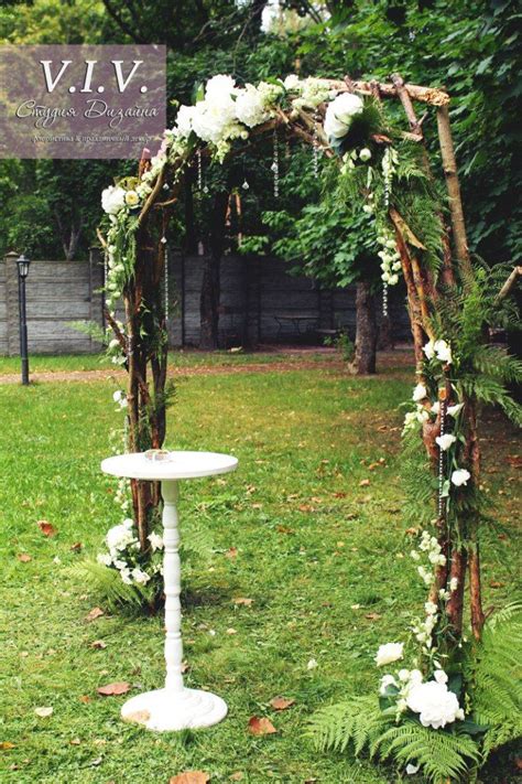 An Outdoor Wedding Arch With White Flowers And Greenery On The Grass In