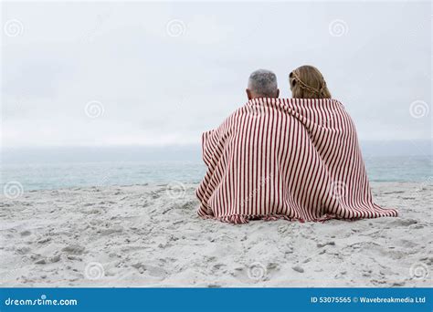 Happy Couple Sitting On The Sand With Blanket Around Them Stock Image