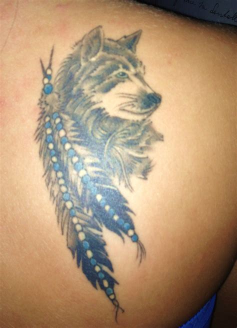 The Back Of A Womans Shoulder With A Wolf And Feathers Tattoo On It