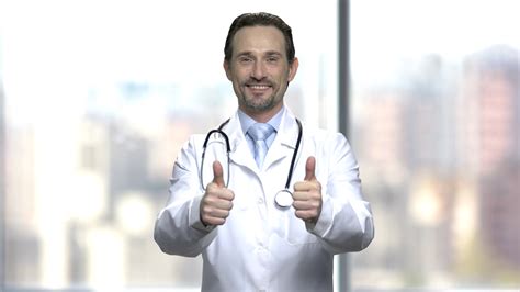 Smiling Caucasian Doctor Giving Two Thumbs Up Happy Male Physician Looking At Camera On Blurred