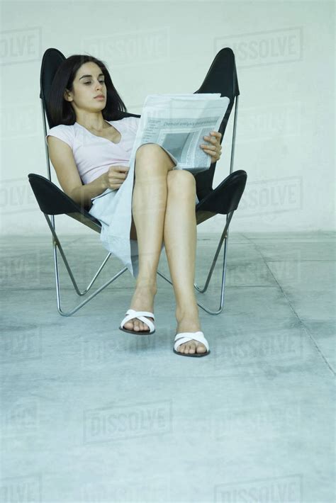 Young Woman Sitting In Chair With Legs Crossed Reading Newspaper Full Length Portrait Stock