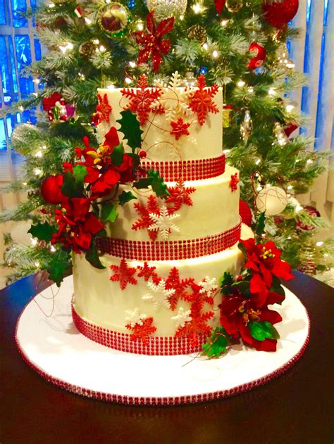 A Three Tiered Cake Decorated With Poinsettis And Holly On A Table In