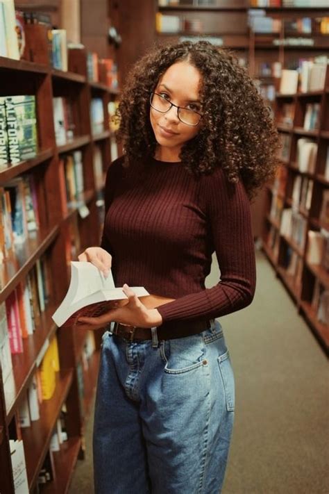 A Woman Standing In A Library Holding A Book