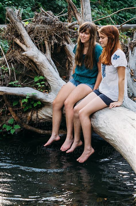 two girls on a log dangling feet in creek by stocksy contributor deirdre malfatto stocksy