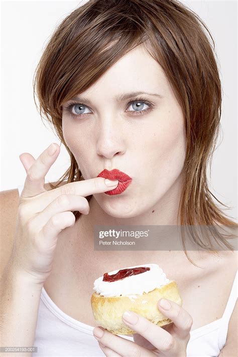 Young Woman Licking Finger Holding Jam And Cream Scone