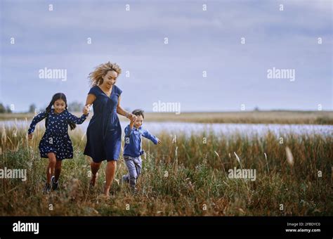 Madre Sujetando Las Manos Mientras Corría Con Su Hija Y Su Hijo En La Hierba Fotografía De Stock
