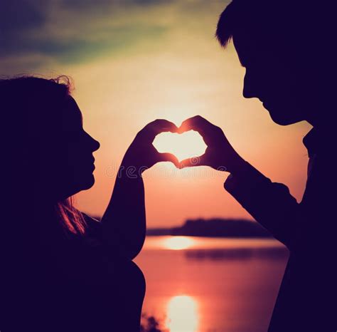 Couple Doing Heart Shape With Their Hands On Lake Shore Stock Photo