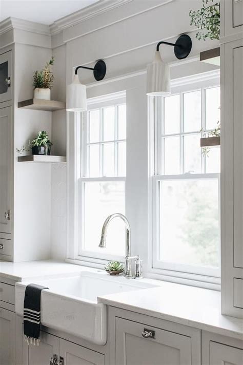 A White Kitchen With Two Windows And Some Plants On The Window Sill