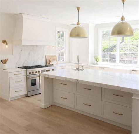 A Large White Kitchen With Marble Counter Tops And Gold Pendant Lights