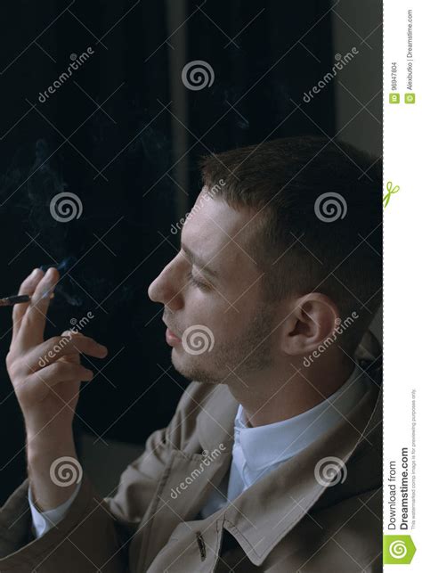 A Handsome And Lonely Guy In A Cloak With A Cigarette Stock Photo