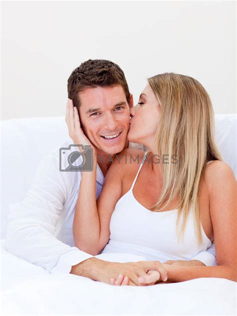 Intimate Woman Kissing Her Husband Sitting On Bed By Wavebreakmedia