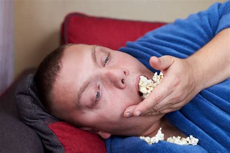 Fat Man In A Robe Eating Popcorn While Lying On The Couch Stock Photo