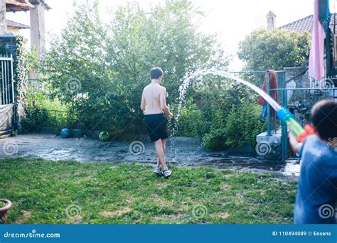 Children Play In The Garden With Guns And Water Rifles On A Sunny