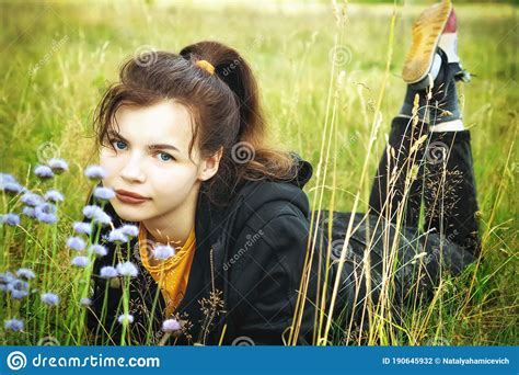 A Young Beautiful Girl Is Resting In The Summer In A Field With Flowers